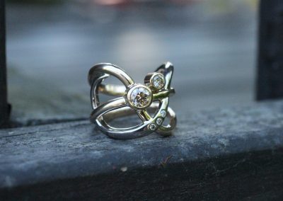 Bred ring lavet af flere tråde der krydser hinanden med en stor champagnefarvet diamant og flere små diamant i en af trådene.