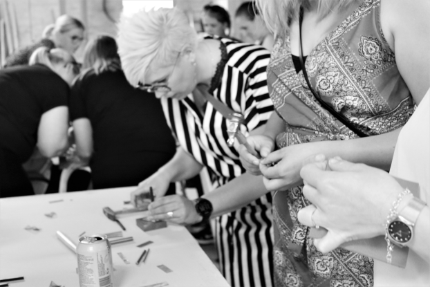 En gruppe af kvinder, som står ved bord med hamre i hånden og er ved at lave smykker.