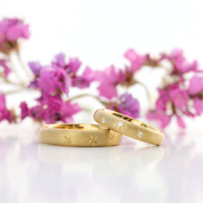 stjernehimmel vielsesringe i guld med blomster i baggrunden