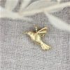 kolibri vedhæng i guld med diamant øjne liggende på hør underlag